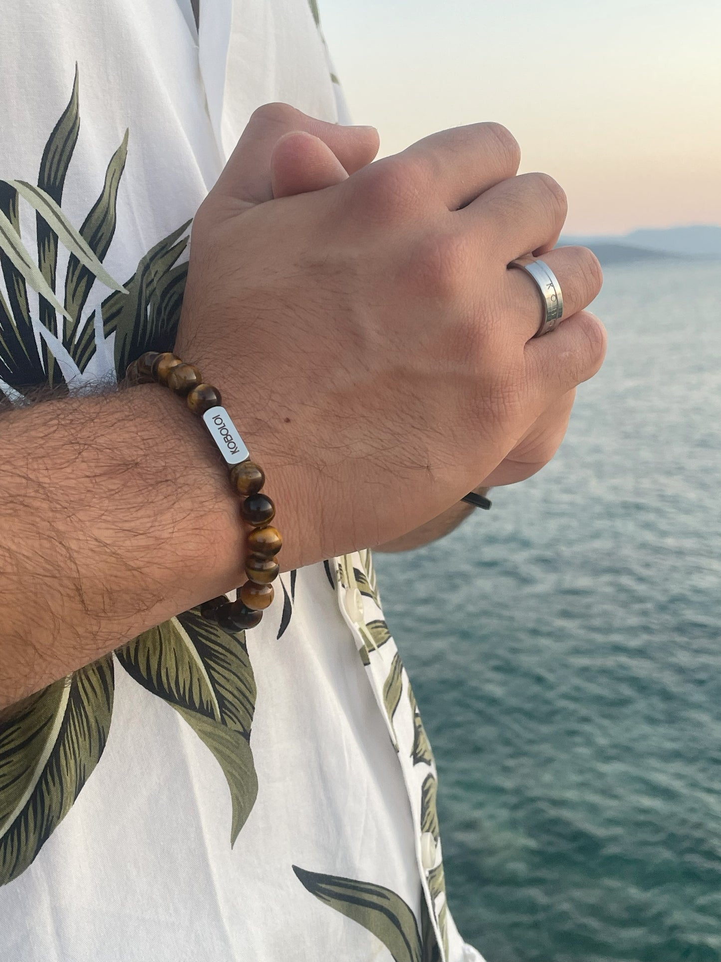 Photo plan rapproché bracelet perles pierres naturelles Œil de Tigre devant la mer.